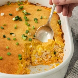 a person holding a spoon in a casserole dish.