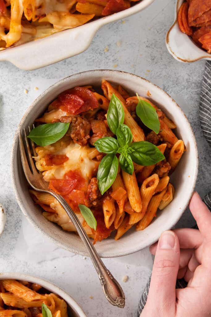 a person holding a bowl of pasta with meat sauce and basil.