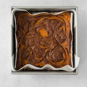 a brownie in a metal pan on a white surface.