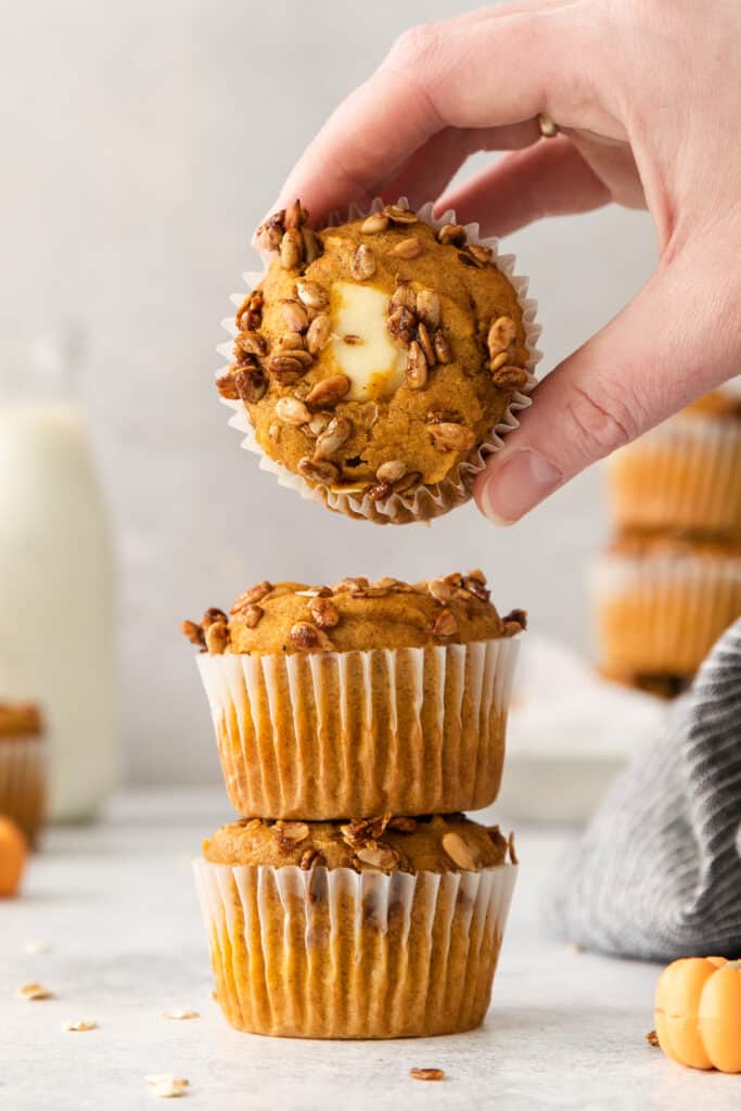 a hand is reaching into a stack of pumpkin muffins.