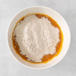 a white bowl filled with flour on a white surface.