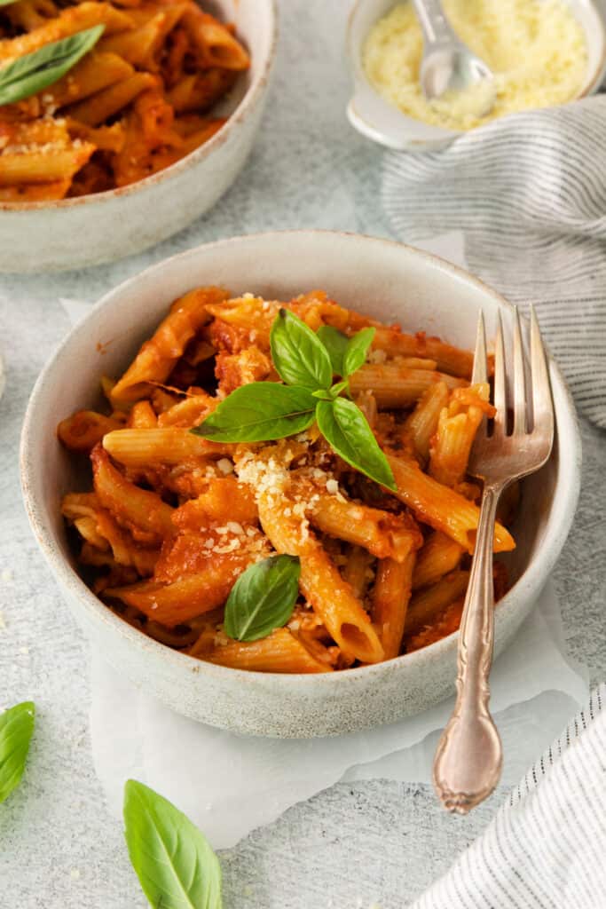 two bowls of pasta with basil and parmesan cheese.