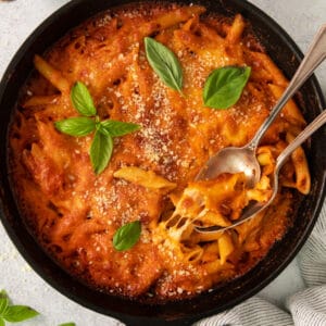 a skillet filled with pasta and sauce with a spoon.