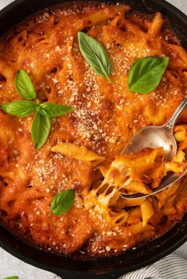 a skillet filled with pasta and sauce with a spoon.