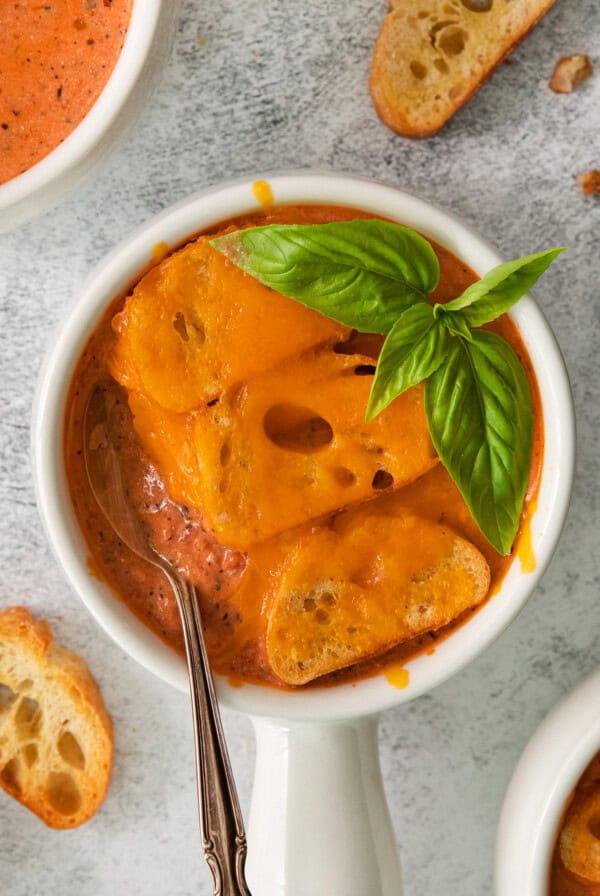 a bowl of tomato soup with bread and basil.