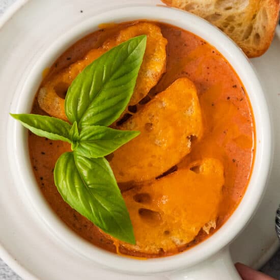 a bowl of tomato soup with bread and basil.