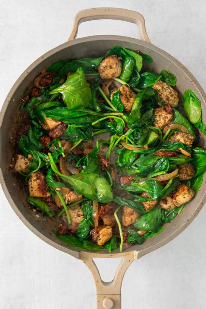 a pan with spinach and chicken in it.