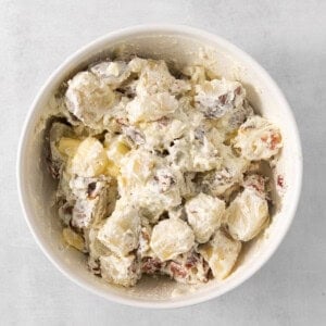 potato salad in a white bowl on a grey background.