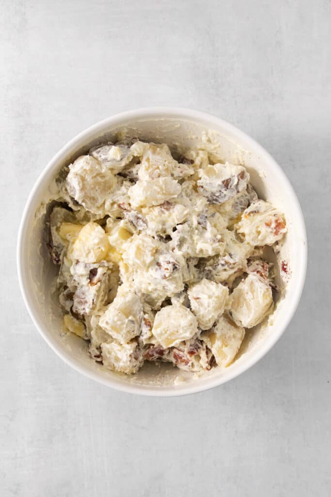 potato salad in a white bowl on a grey background.