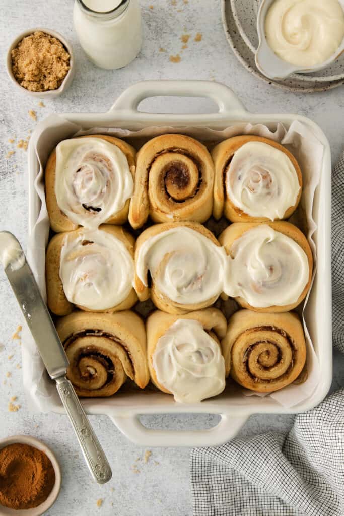 a pan filled with cinnamon rolls next to a glass of milk.