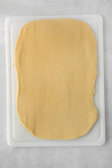 a square shaped dough on a white cutting board.