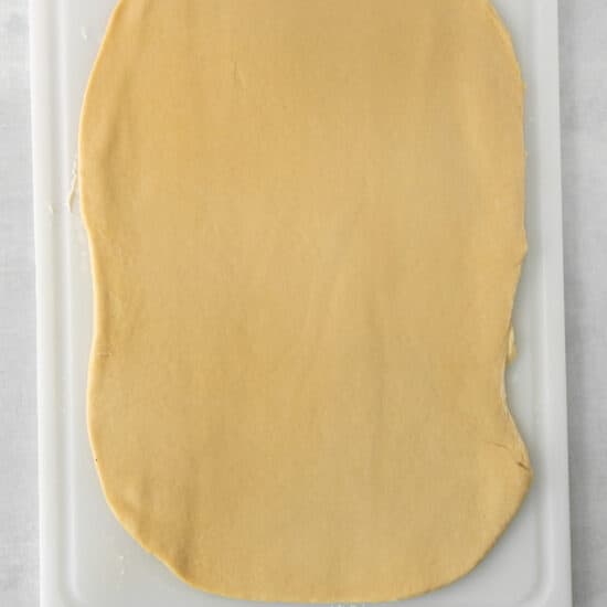 a square shaped dough on a white cutting board.
