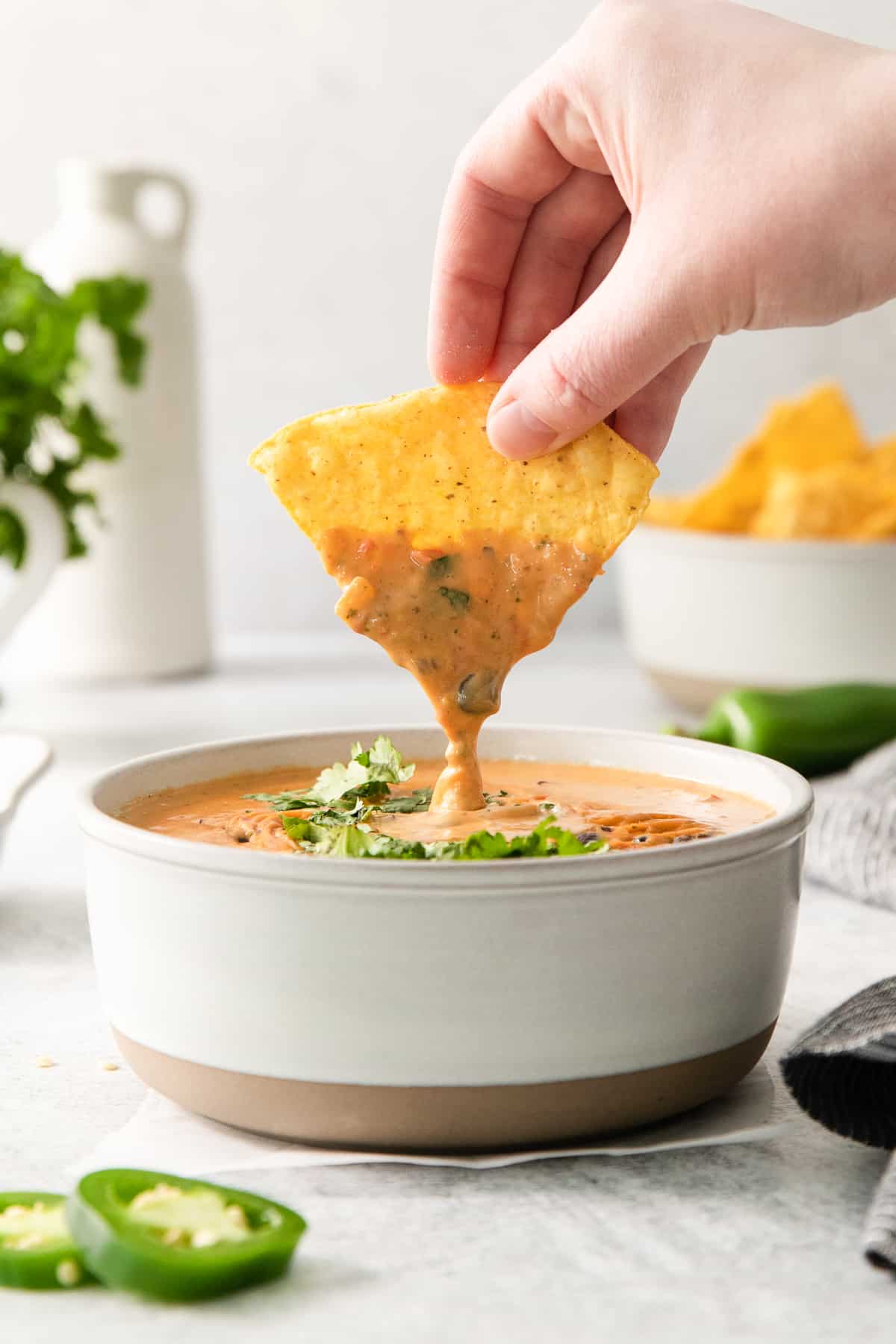 a hand dipping a tortilla chip into a bowl of tortilla soup.