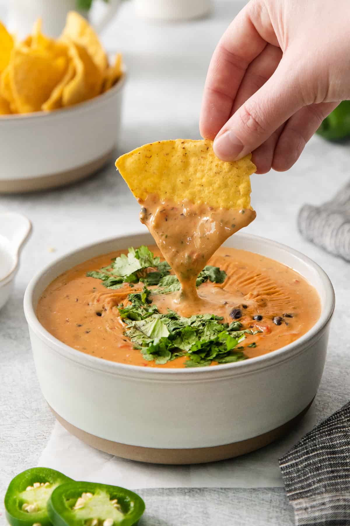 a person dipping a tortilla chip into a bowl of salsa.