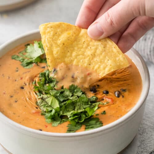 a hand dipping a tortilla chip into a bowl of quesadilla.