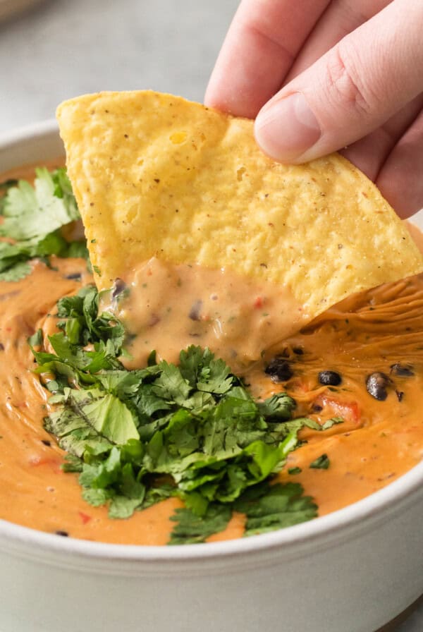 a hand dipping a tortilla chip into a bowl of quesadilla.