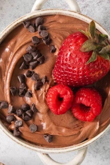 a bowl of chocolate pudding with a strawberry and chocolate chips.
