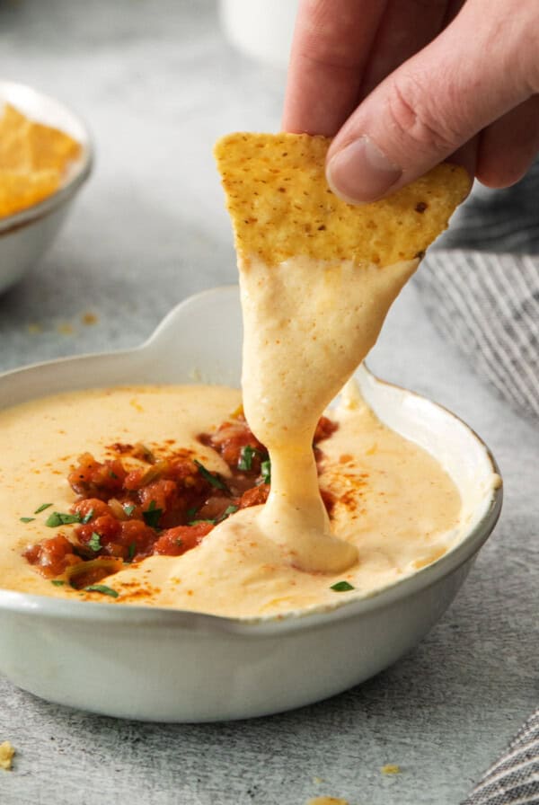 a person dipping a tortilla into a bowl of dip.