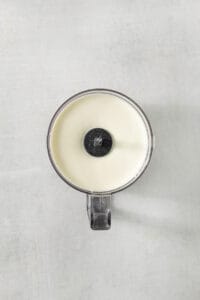 a white candle with a black lid sitting on a white surface.