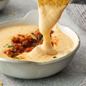 a tortilla chip being dipped into a bowl of cheese dip.