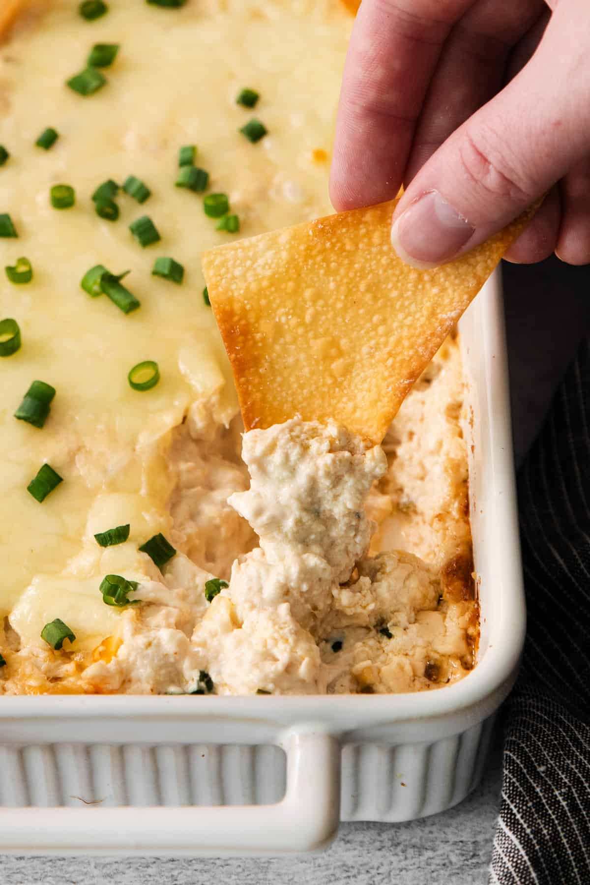 a hand dipping into a dish of chicken dip.