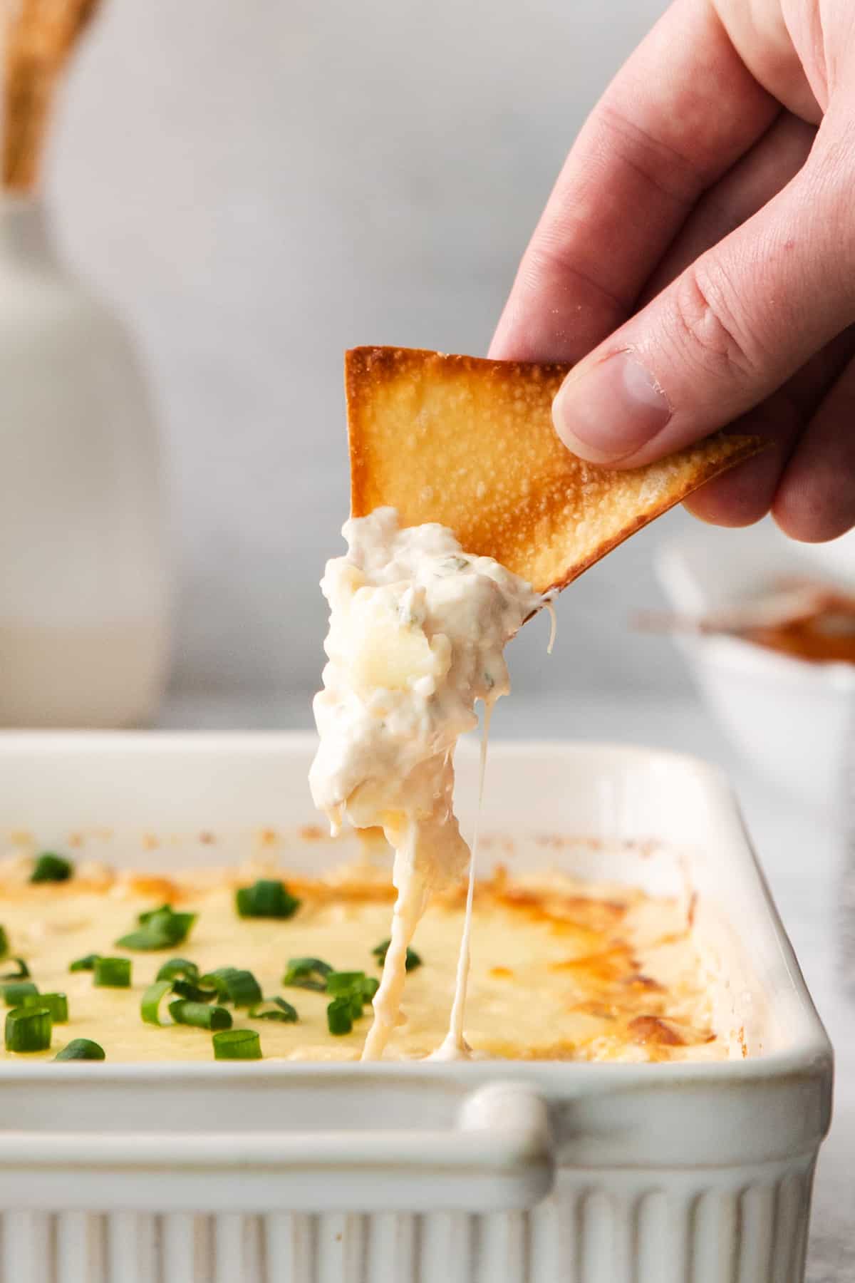 a person dipping a cracker into a dish of dip.