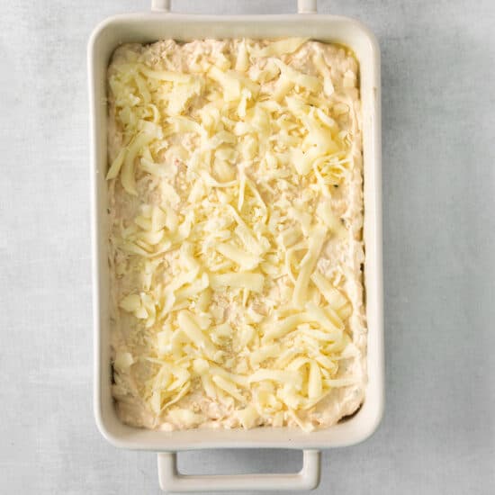 a white baking dish with a layer of cheese on it.