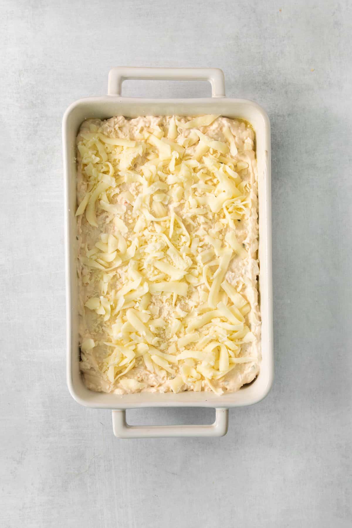 a white baking dish with a layer of cheese on it.