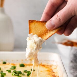 a person dipping a cracker into a dish of cheese dip.