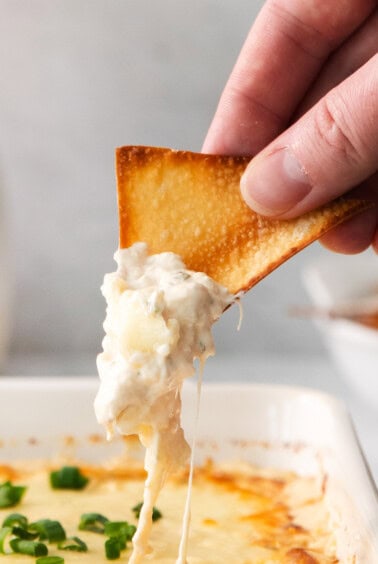 a person dipping a cracker into a dish of cheese dip.