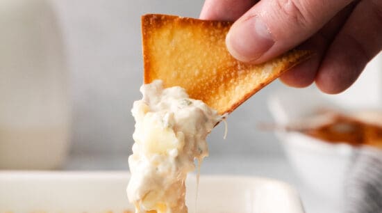 a person dipping a cracker into a dish of cheese dip.
