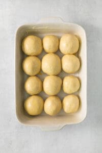 a white baking dish filled with dough balls.
