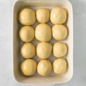 a white baking dish filled with dough balls.