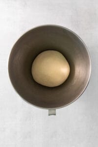 a ball of dough in a metal bowl on a white background.
