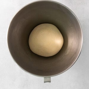 a ball of dough in a metal bowl on a white background.