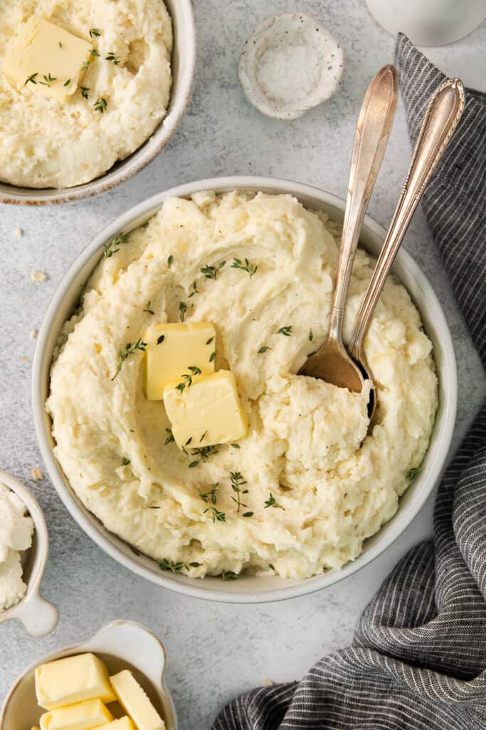 Two bowls of mashed potatoes with butter and herbs.