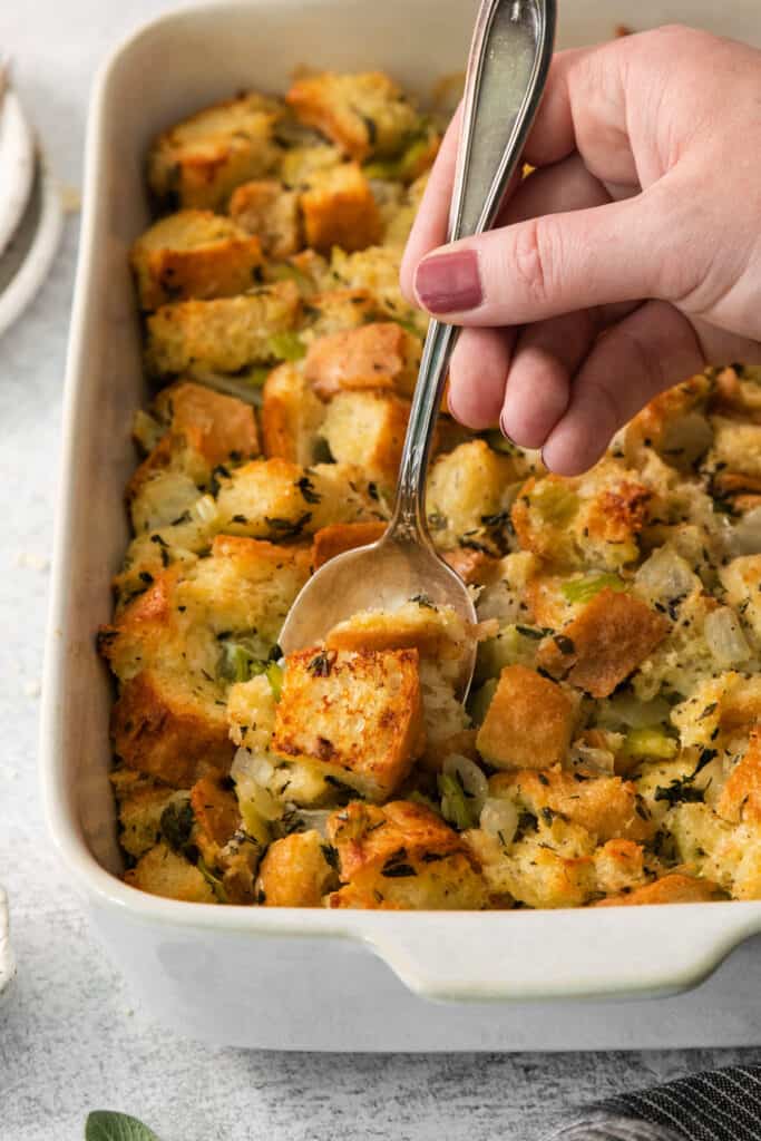 A person scooping stuffing out of a baking dish.