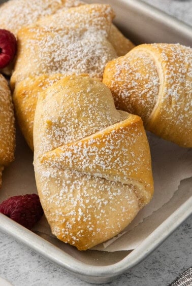 a tray of cinnamon rolls with raspberries and powdered sugar.