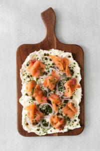 smoked salmon pizza on a wooden cutting board.