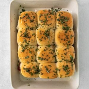 Cheesy sliders in a white dish with herbs.