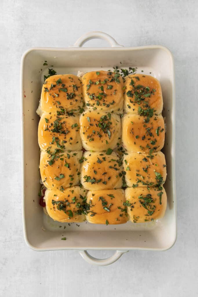 Cheesy sliders in a white dish with herbs.