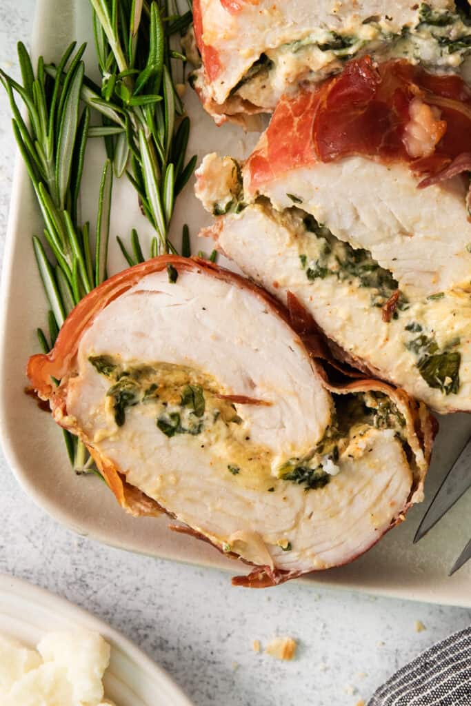 A white plate with stuffed chicken and sprigs of rosemary.