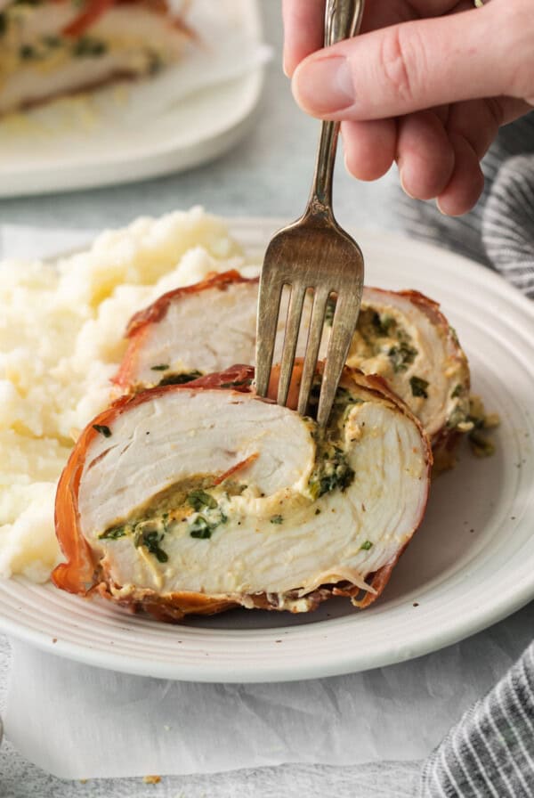 A person holding a fork over a plate of stuffed turkey with mashed potatoes.