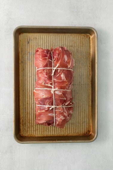 Ham wrapped in bacon on a baking sheet.