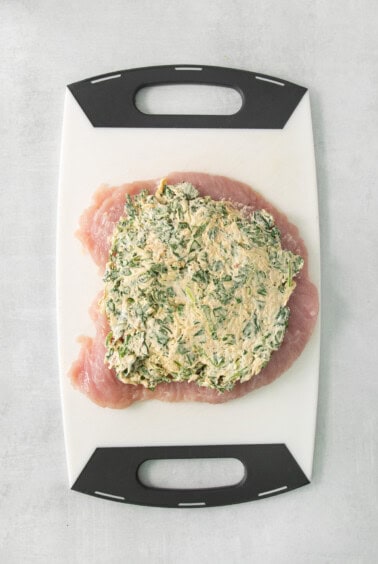 Chicken breast with spinach on a cutting board.