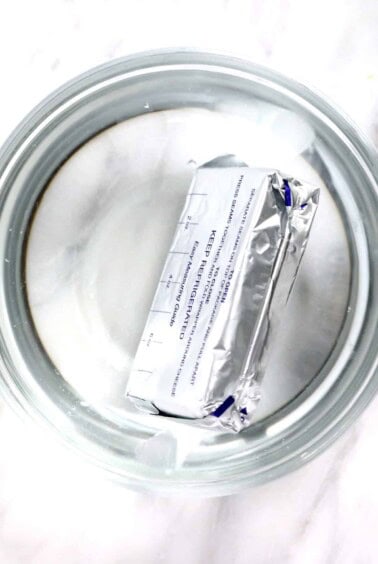 A glass bowl covered with plastic wrap for softening cream cheese.