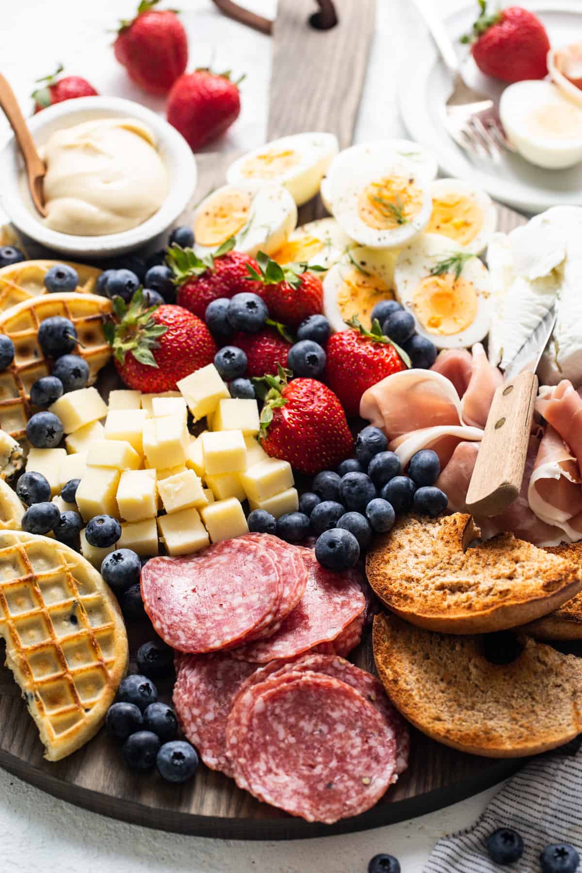 A platter with a variety of meats, cheeses, fruits and waffles.