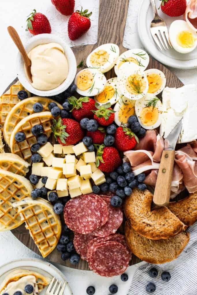 A platter with a variety of meats, cheeses, fruits and waffles.