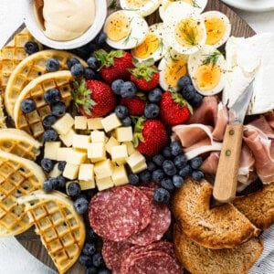 A platter with a variety of meats, cheeses, fruits and waffles.