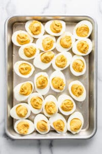 Deviled eggs on a baking sheet with mustard.